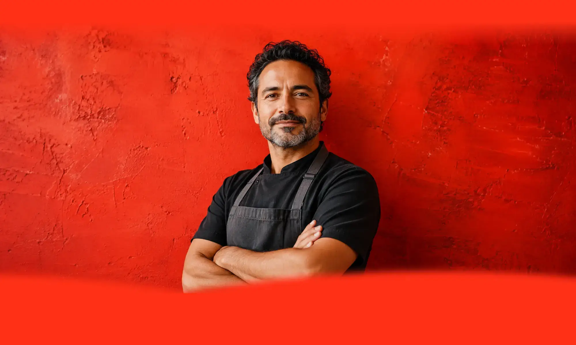 Confident small-business owner standing with arms crossed in front of a bold red wall