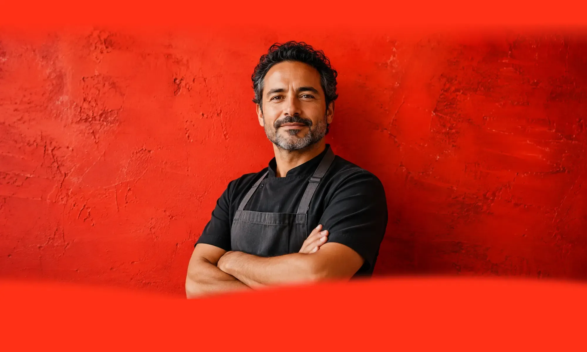 A confident small business owner in a black apron standing against a bold red wall