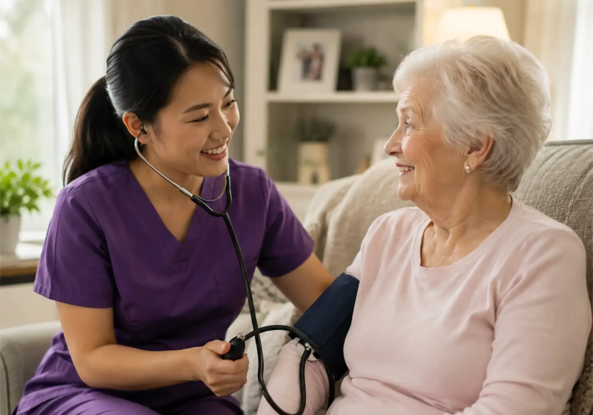 A smiling home-health nurse checking an elderly woman's blood pressure in her living room